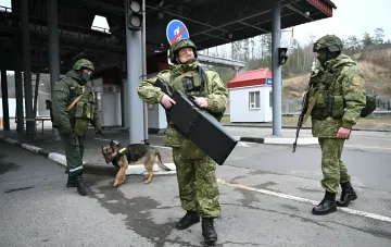 Пограничники в камуфляже с собакой и баллистическим щитом на контрольно-пропускном пункте в пограничной зоне
