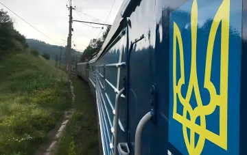 Пассажирский поезд «Укрзализныци» с логотипом на борту на фоне холмистой местности