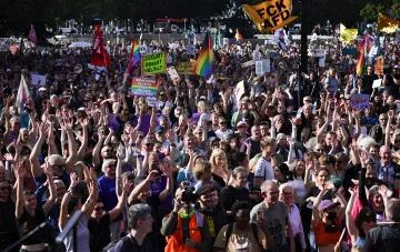 Толпа протестующих на митинге против партии AfD в Германии, участники поднимают руки и держат радужные флаги и плакаты