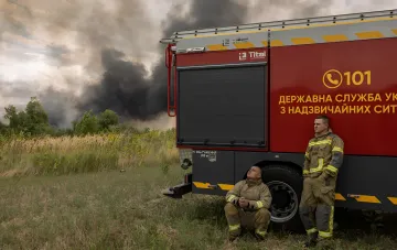 Пожарные отдыхают у пожарной машины на фоне дыма от горящего поля на Житомирщине