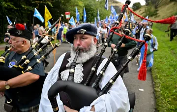 Scottish musicians in traditional attire playing bagpipes during a national parade with Scottish flags