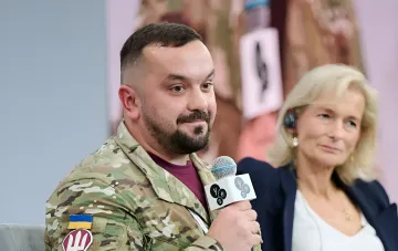 Начальник ПВО 7-го корпуса ДШВ в камуфляже с украинским флагом на рукаве выступает с микрофоном на панельной дискуссии