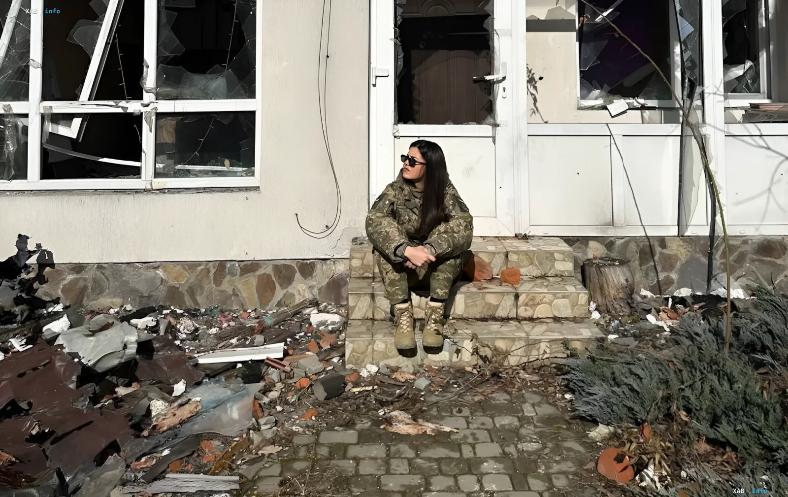 Военнослужащая в камуфляжной форме сидит на ступенях разрушенного дома и задумывается о будущем после службы