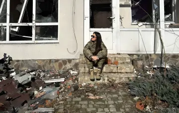 Военнослужащая в камуфляжной форме сидит на ступенях разрушенного дома и задумывается о будущем после службы