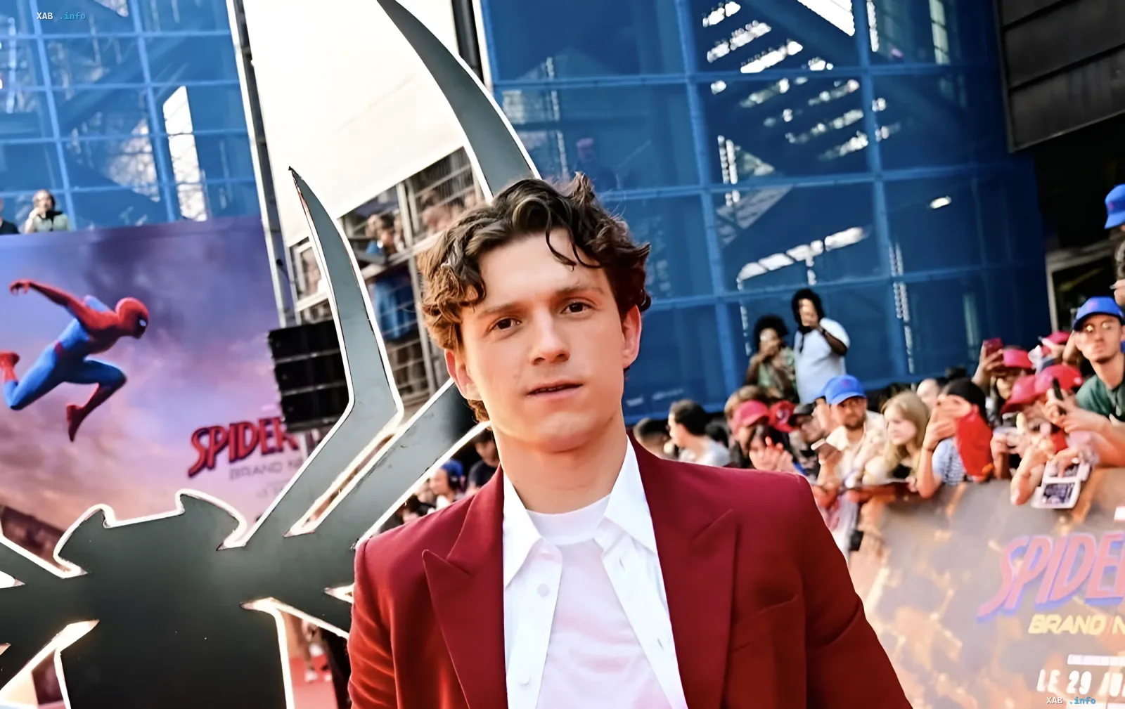 Tom Holland in rotem Sakko bei der Spider-Man-Film-Premiere vor dem Spider-Man-Logo
