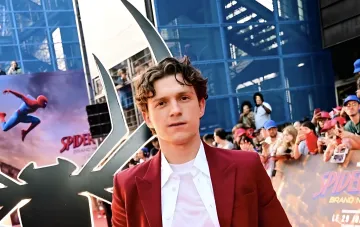 Tom Holland in rotem Sakko bei der Spider-Man-Film-Premiere vor dem Spider-Man-Logo