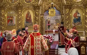 Богослужіння в храмі на свято Воздвиження Хреста Господнього: архиєрей у мітрі та священнослужителі в червоних одежах біля вівтаря з хрестом
