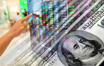 Dollar-Kurs und Währungsmarkt: Eine Hand zeigt auf ein Börsenbildschirm mit Kursen vor Hundert-Dollar-Scheinen