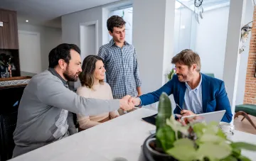 Eine Familie von intern vertriebenen Personen schließt über einen Händedruck einen Kaufvertrag für eine Wohnung mit Wohngutschein und Hypothek ab