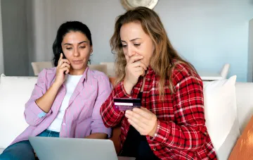 Zwei Frauen betrachten besorgt eine Bankkarte und einen Laptop, während sie unbefugte Abbuchungen besprechen