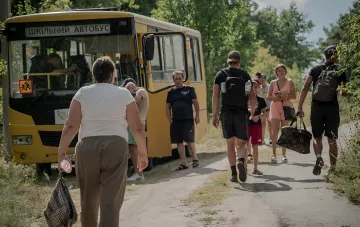 Шкільний автобус і люди з багажем під час евакуації дітей у Донецькій області