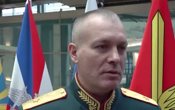 General Grunis in a ceremonial military uniform with gold epaulettes against the Russian tricolor and a red service flag — a 'Hero of Russia' who reported the capture of Kostyantynivka