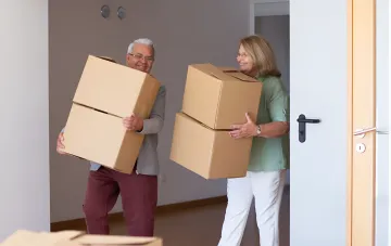 Älteres Paar trägt Kartons beim Umzug in eine neue Wohnung vor dem Hintergrund steigender Preise für Einzimmerwohnungen in ukrainischen Regionalzentren