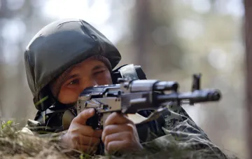 Ukrainischer Soldat mit Gewehr in Tarnkleidung im Wald: Diskussion über Rückkehr aus SZZ nach vereinfachtem Programm