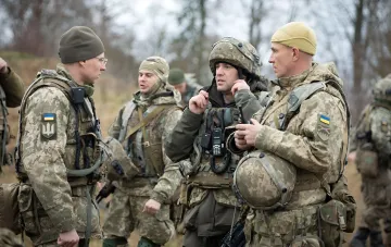 Бійці ЗСУ в камуфляжній формі з нашивками на тлі осіннього лісу обговорюють тактичні завдання