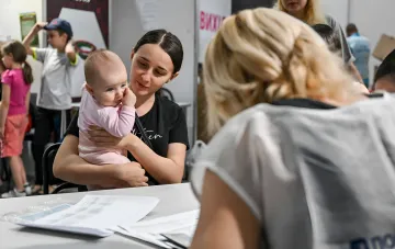 Young mother holding a baby interacts with an organization staff member at a document processing desk
