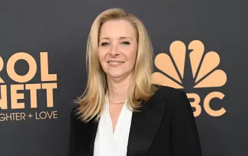 Лиза Кудроу в чёрном пиджаке и белой блузке на фоне логотипа NBC — образ, который она выбрала для выхода на «Эмми» вместе с сыном