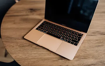 Золотистый MacBook на деревянном столе: трекпад и клавиатура в контексте новых жестов macOS 27 Golden Gate