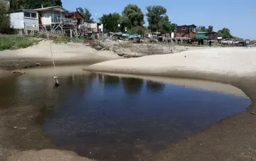 Пересохшее русло малой реки в Украине: мелкая вода, песчаные отмели и дома на берегу на фоне исторического минимума уровня воды
