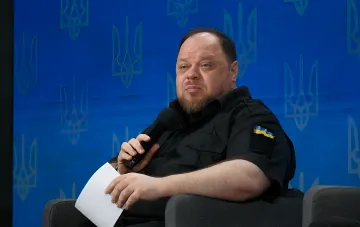 Стефанчук с микрофоном на фоне синего экрана с тризубами обсуждает давление на финансирование войны Россией