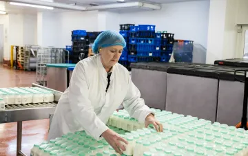 Украинская работница на молочном производстве в Польше сортирует бутылки на конвейере — иллюстрация к статье о схемах обмана трудовых мигрантов