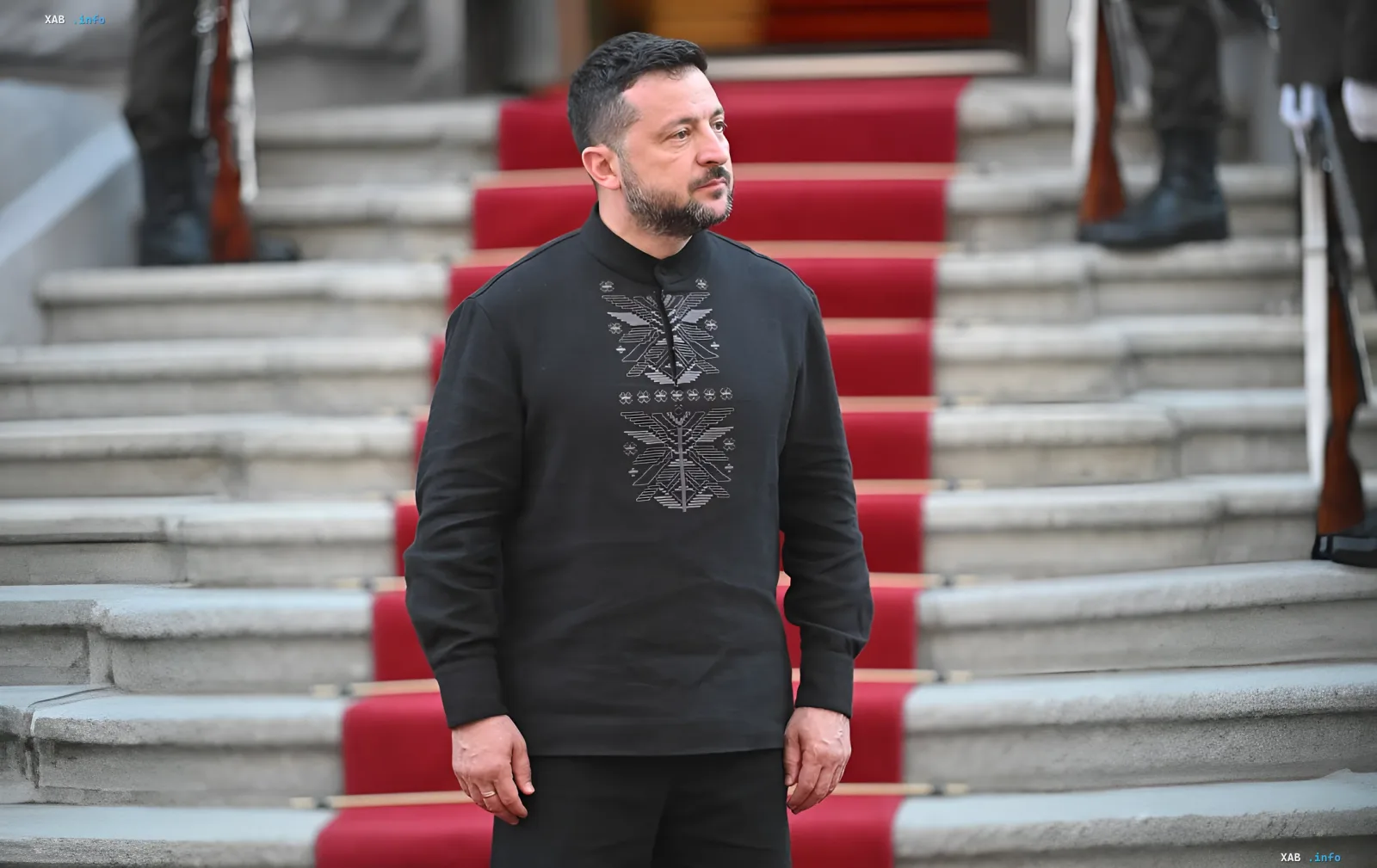 Volodymyr Zelensky in a black embroidered shirt against stone steps with a red carpet and honour guard — trust rating drops to 54% in KIIS poll