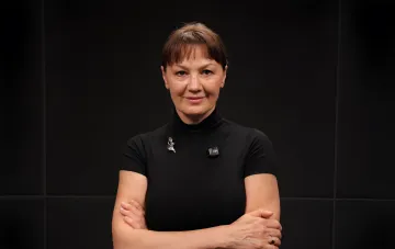Лариса Руснак у чорному водолазці зі схрещеними руками на темному тлі — портрет до інтерв'ю про «Одіссею Маріуполя», фільм «Хатник» і силу, народжену з втрати