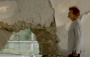 A woman by a damaged wall in a frame from the documentary 'Traces', submitted by Ukraine for the 2027 Oscars