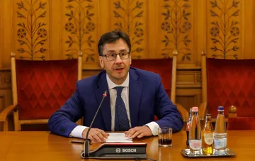 Hungarian official speaks at a negotiation table with a Bosch microphone in a formal hall, discussing the request for an exemption from Russian oil sanctions