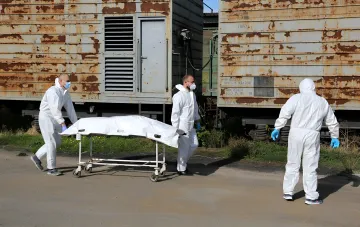 Workers in protective suits transport a repatriated body on a stretcher near railway wagons for identification