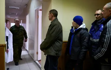 Чоловіки, включно зі співробітником у камуфляжному форму, стоять у коридорі установи на тлі обговорення загрози нової мобілізації в Росії