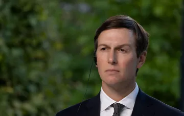Jared Kushner im Anzug mit Kopfhörer-Mikrofon vor grünem Blattwerk bei einem öffentlichen Auftritt, der die Versprechen Putins zur Eroberung des Donbas kritisiert