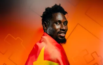 Schachtar-Stürmer Lassin Traore mit der Flagge der DR Kongo vor orangefarbenem geometrischem Hintergrund