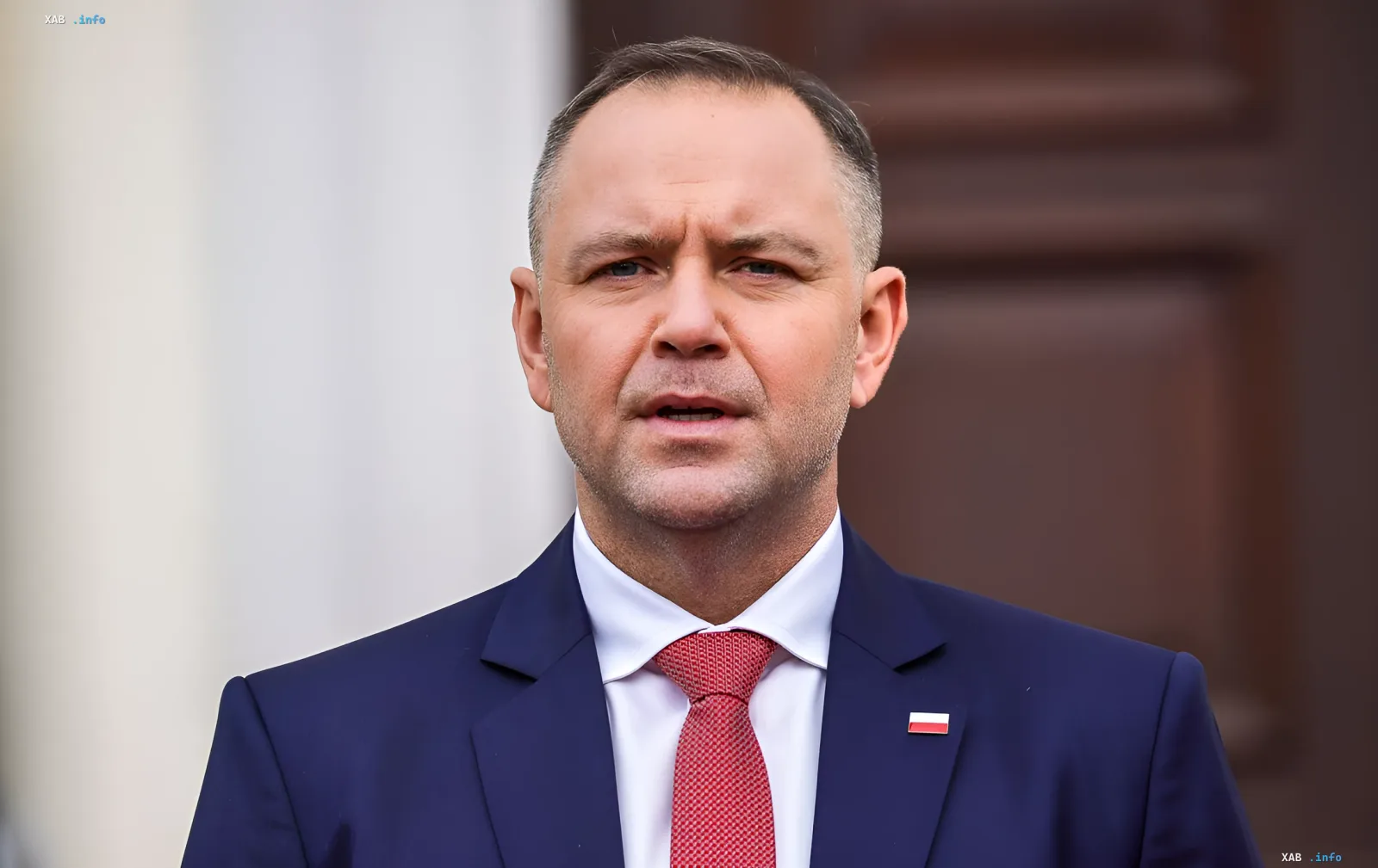 Польский политик Навроцкий в синем костюме с красным галстуком и значком флага Польши на лацкане, на фоне резкого заявления о территории и конфликта с Туском