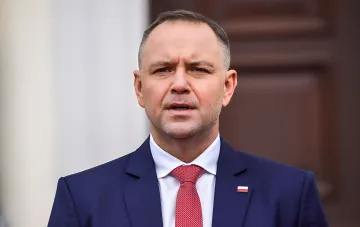 Польский политик Навроцкий в синем костюме с красным галстуком и значком флага Польши на лацкане, на фоне резкого заявления о территории и конфликта с Туском