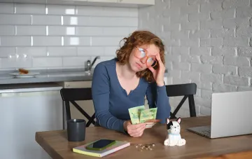 A worried woman counts Ukrainian hryvnia notes at a desk with a laptop amid the NBU rate hike to 16% and rising loan costs