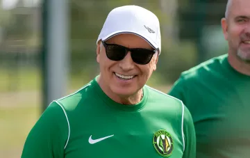 President of Polissya in the club's green kit and white cap smiles on the stands during a UPL match, in the break of which a chess duel with the head of Veres took place
