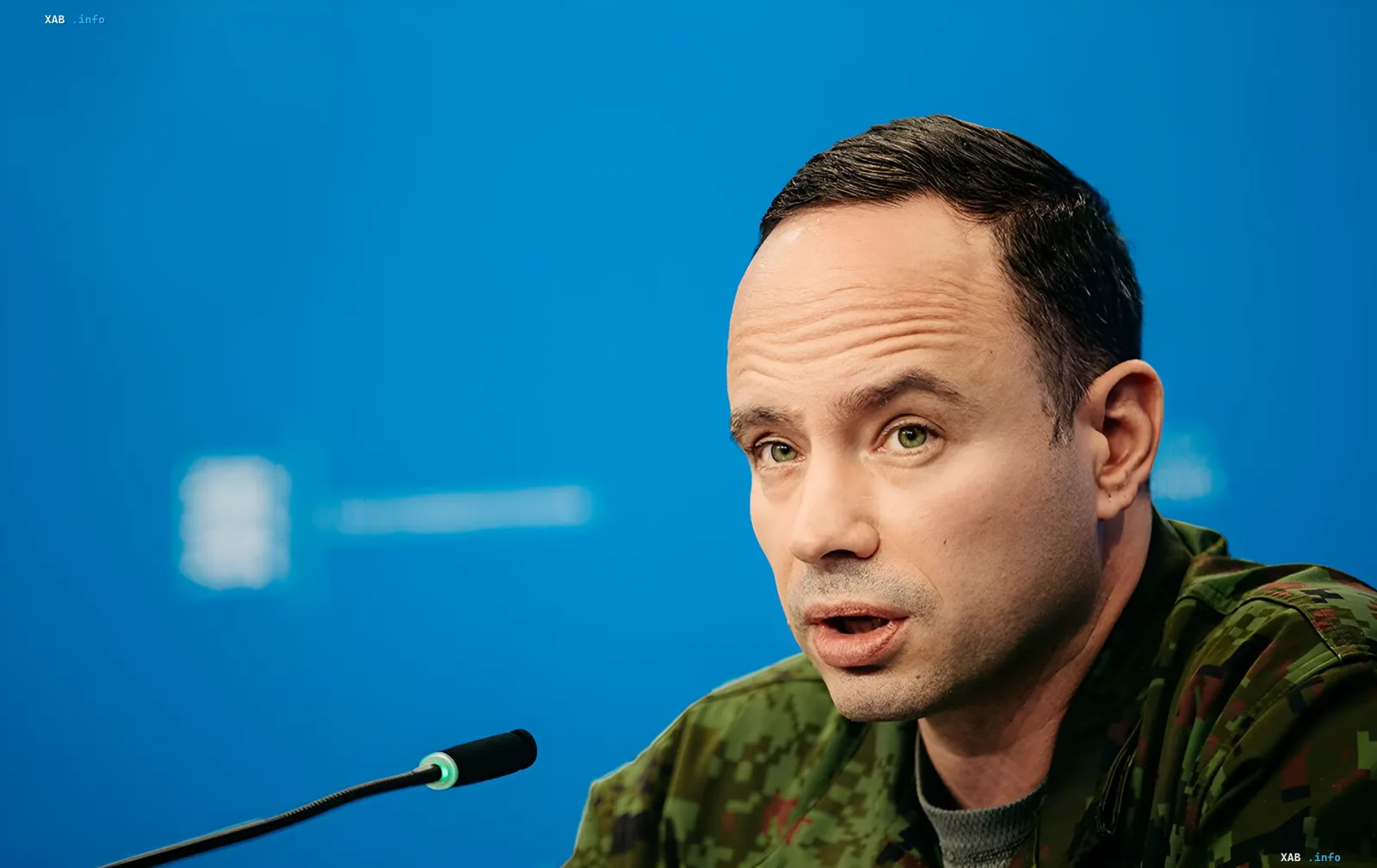 Official in camouflage uniform speaking at a briefing with a microphone against a blue screen backdrop — context for reports on Russian military losses per Estonian intelligence