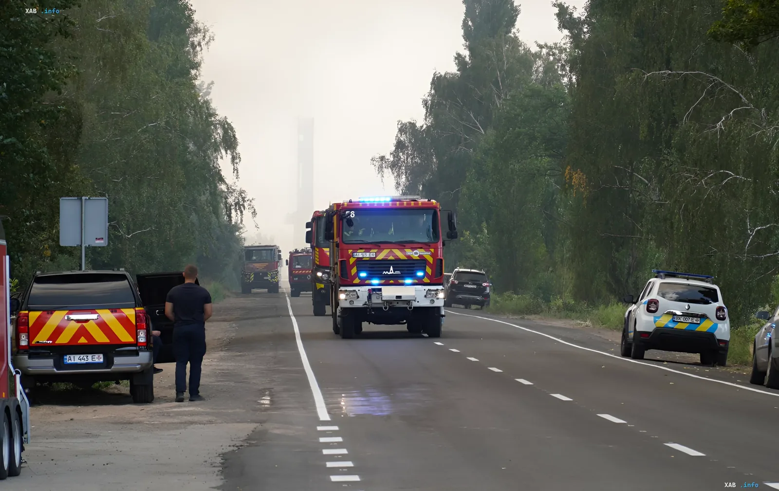 Convoy of fire trucks with flashing lights heading toward a smoky fire scene on a rural road — Kyiv city administration warns of smoke over the right bank