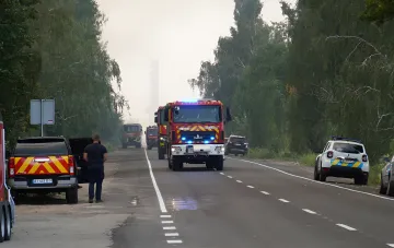 Convoy of fire trucks with flashing lights heading toward a smoky fire scene on a rural road — Kyiv city administration warns of smoke over the right bank