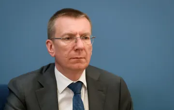 Президент Латвии на фоне синей стены в деловом костюме и очках, комментируя отставание Европы в перестройке ПВО под войну дронов