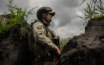 Український військовий у камуфляжі та шоломі зі стрілецькою зброєю в окопі на Сумщині, лінія фронту