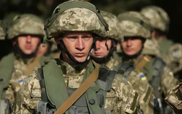 Бієць ЗСУ в цифровому камуфляжі на фоні строю українських військовослужбовців