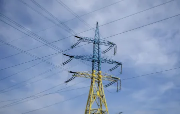 High-voltage electricity transmission tower in blue and yellow against a cloudy sky, symbolizing Ukraine's energy infrastructure amid the shift to a European price-cap model