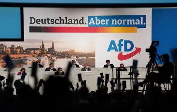 Съёмка экзитполов партии АдН (AfD) в Германии: журналисты с камерами перед сценой с логотипом партии и лозунгом «Deutschland. Aber normal.»