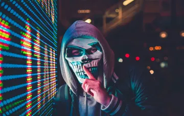 Hacker in a hood and skull mask against neon digital data — symbol of the Poseidon cyber operation by Ukrainian hackers who stole the Russian fleet's design database