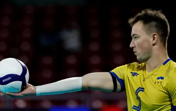 Spieler der ukrainischen Volleyball-Nationalmannschaft im gelben Trikot hält einen Ball auf der Hand vor der Tribüne