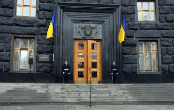 Здание Кабинета Министров Украины с флагами и охраной на фоне призыва экономиста к централизации военного экономического управления в условиях стагфляции
