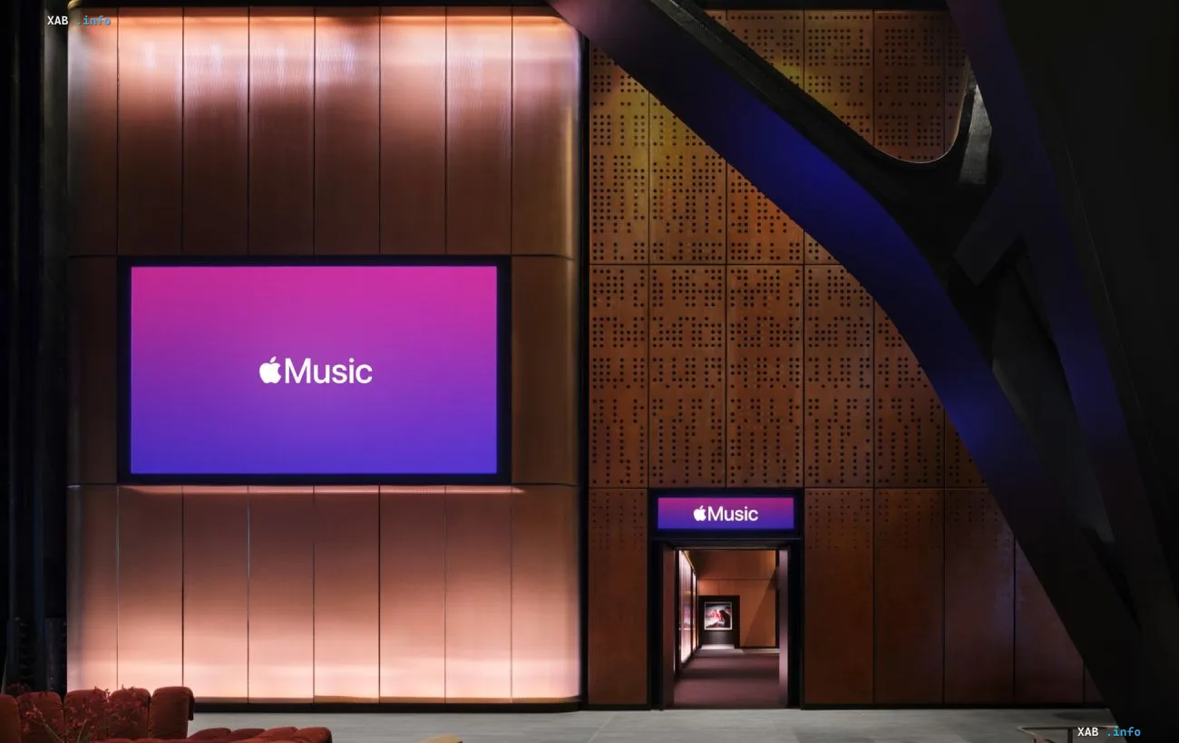 Интерьер концертного зала Apple Music Hall в Лондоне: большой экран с логотипом Apple Music, вход в зал и медные архитектурные панели