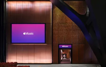 Интерьер концертного зала Apple Music Hall в Лондоне: большой экран с логотипом Apple Music, вход в зал и медные архитектурные панели